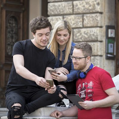 A group of three students standing in front of TU Graz old campus while chatting.